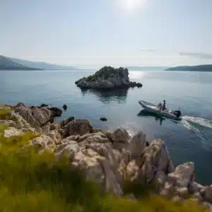 A calming seascape with rocky shorelines and a motorized inflatable boat with two people under a lightly clouded sky.