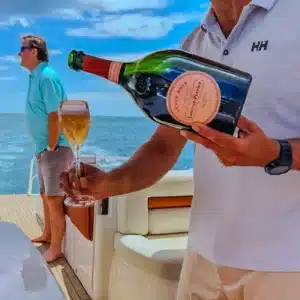 Person pouring champagne into a flute glass on a yacht, with ocean and marine seating in the background, evoking luxury.