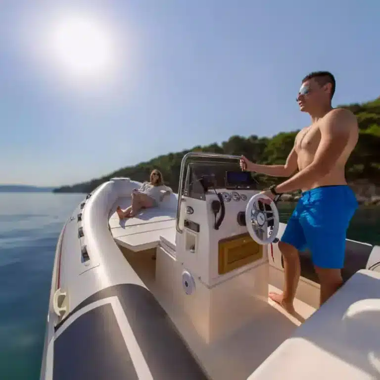 A man at the helm steering the boat and a woman relaxing at the bow, enjoying a sunny day on a calm sea or large lake.