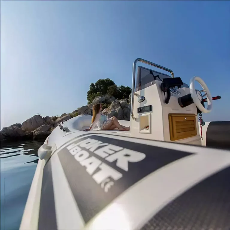 An inflatable boat labeled JOKER BOAT near a rocky coastline with a person looking out on a calm, clear day.