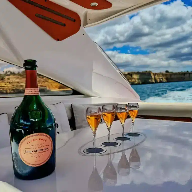 Bottle of Laurent-Perrier Cuvée Rosé champagne with four filled flutes on a boat set against a coastline during a yacht excursion.