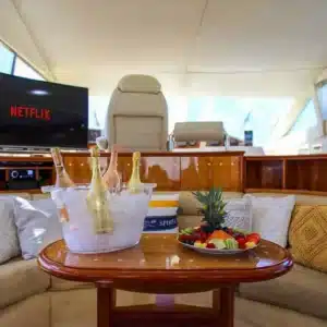 Luxurious yacht with an elegant wooden table displaying champagne and fresh fruit, set against a plush seating area with a Netflix-enabled TV.