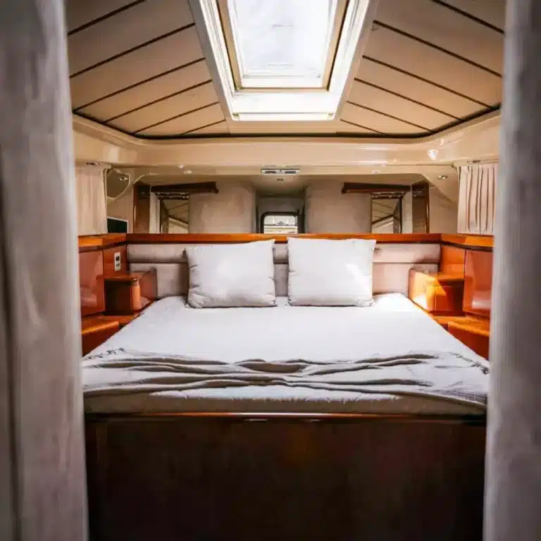 Cozy yacht cabin interior with a large bed, warm wood cabinetry, and natural light from ceiling hatch.