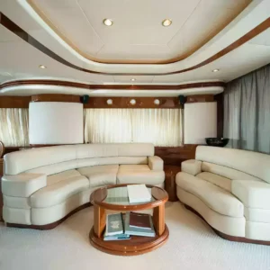 Interior view of a luxurious yacht featuring a cream-colored sofa, matching loveseat, wooden coffee table, and elegant wood paneling.