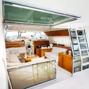 A well-appointed cabin in a luxury yacht showcasing white couches, a coffee table, kitchenette, and elegant decor in neutral shades.