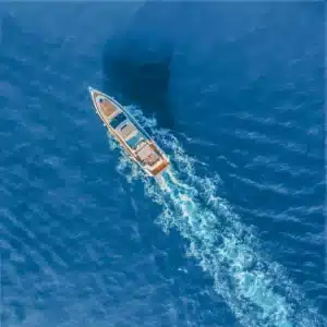 A luxury yacht sailing on calm deep blue sea as seen from above, leaving a trail of wake behind.