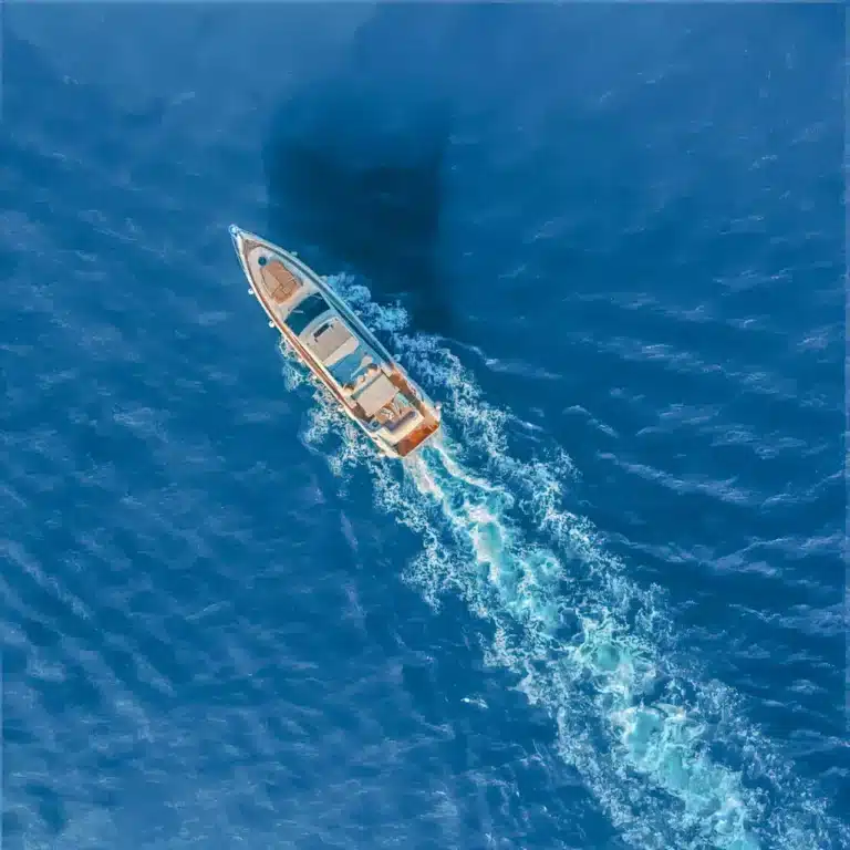 A luxury yacht sailing on calm deep blue sea as seen from above, leaving a trail of wake behind.