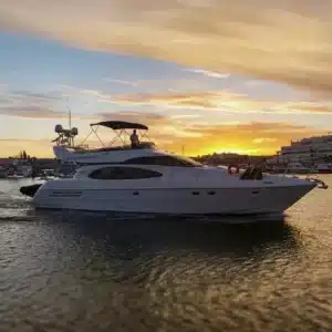 Luxury yacht named Kerry on the water during sunrise or sunset with warm colors, a silhouetted horizon, and a person on the upper deck.