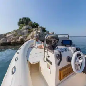 A modern speedboat console with a GPS navigation screen, steering wheel, and a woman enjoying the view on a sunny day with calm seas.