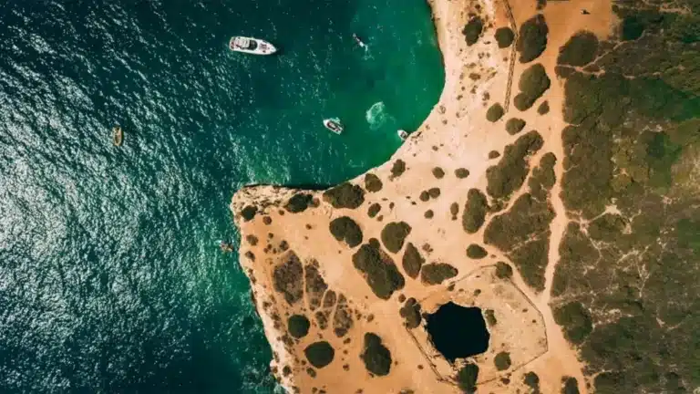 Aerial shot of a coastal landscape with YOLO One yacht near Marina de Vilamoura, showing clear blue-green water and vegetation patches.