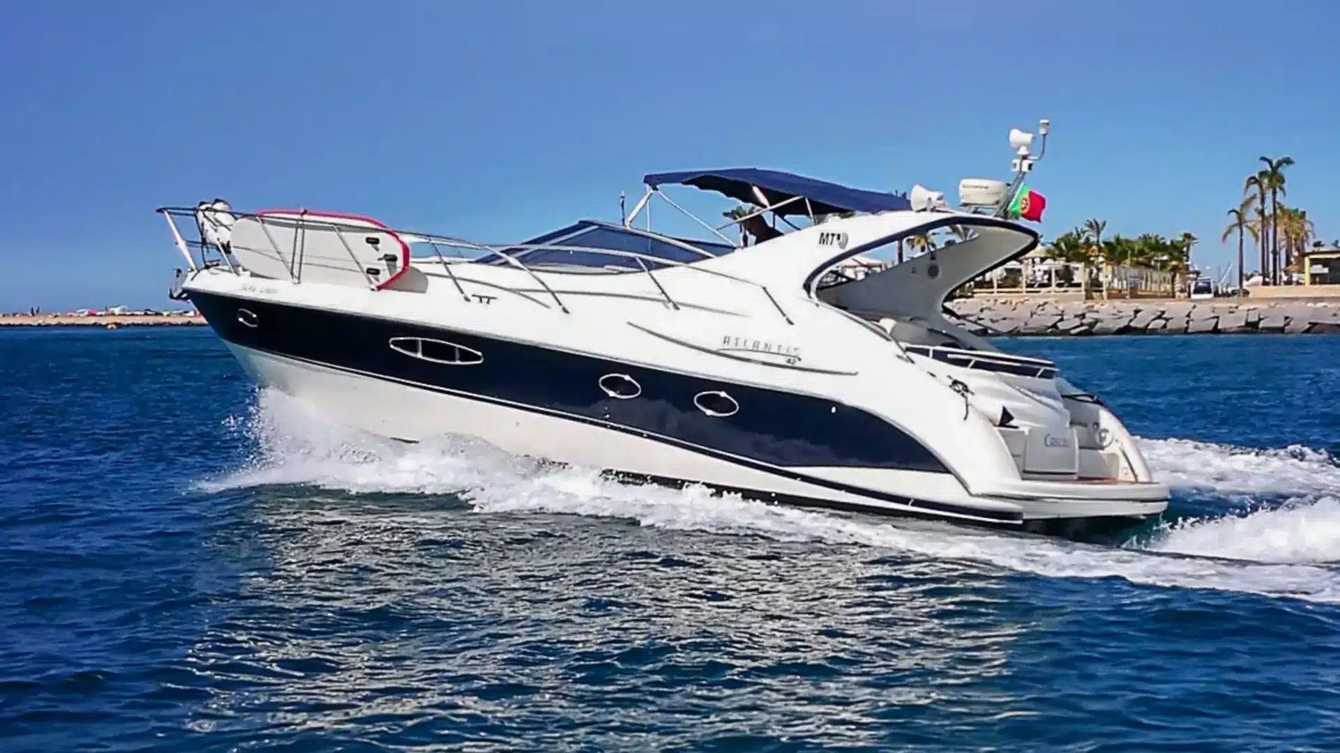 Luxury motor yacht Jacky Louise cruising through clear blue waters near a coastline with palm trees, featuring a white hull and dark blue accents.