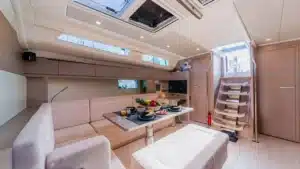 Interior of the Katerina Wings yacht at Cascais Marina showing a plush seating area, dining table with breakfast items, and a staircase to the upper deck.