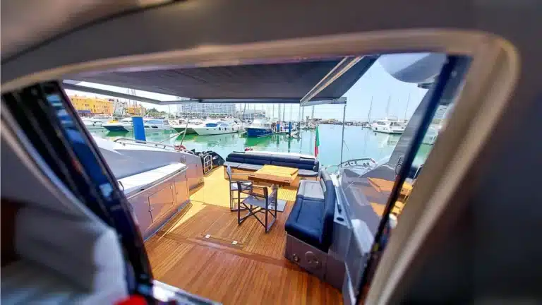 Luxurious view from inside yacht Baco IV looking out towards Marina de Vilamoura with plush seating and canopy shade.