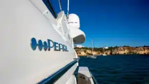 Side view of the luxurious yacht PEARL sailing near Marina de Vilamoura in clear blue waters under a sunlit sky.