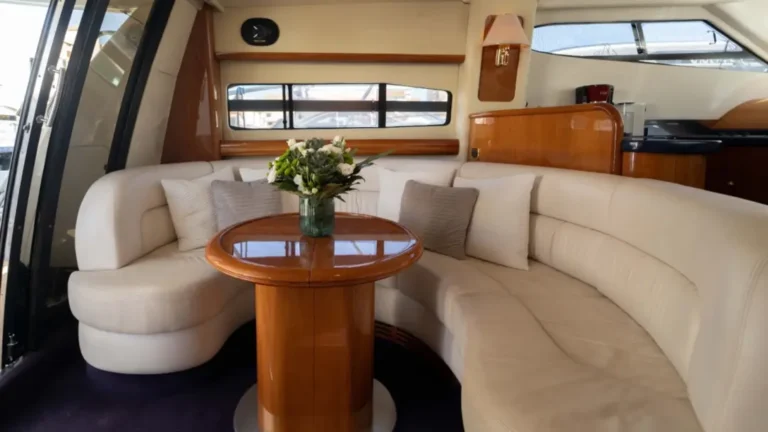 Interior cabin of the Mr Cliff yacht located at Marina de Vilamoura, featuring cream leather seating, polished wooden table, and elegant decor.