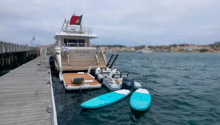 Luxury yacht Katerina XL moored at Cascais Marina in Portugal with paddleboards and houses in the background.