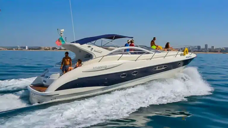 Luxury yacht Jacky Louise cruising with happy passengers near the scenic coastline of Portimão, Faro under clear skies.