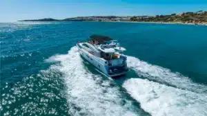 Luxury motor yacht KEV cruising on blue waters near Marina de Vilamoura, capturing speed and elegance with a clear sky and distant coastline.