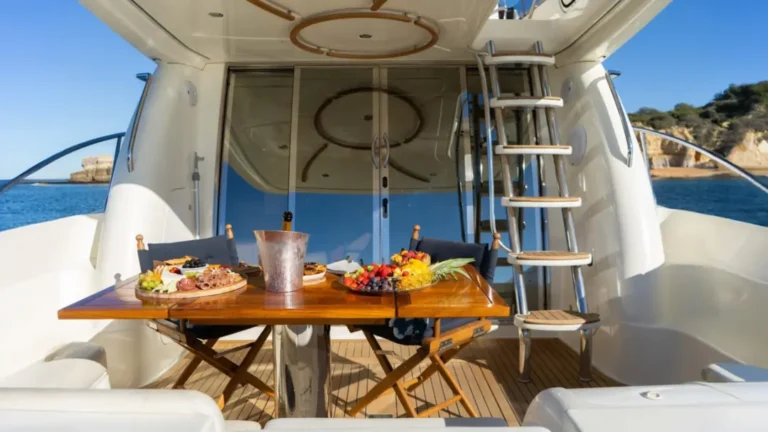 The aft deck of Mr Cliff yacht at Marina de Vilamoura, set for a luxurious dining experience with food, champagne, and sea view.