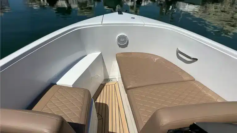 Interior of a luxurious yacht with tan upholstered seating, teak wood deck, speaker system, and stainless steel handrail, docked at Vilamoura Marina.