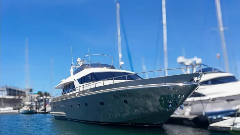 The image shows the luxury yacht Katerina XL moored at a sunny marina alongside other boats, showcasing its sleek design and multiple decks.