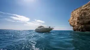 YOLO One luxury yacht cruising near large rocky cliffs in Marina de Vilamoura on a clear, sunny day, perfect for seafaring adventures.