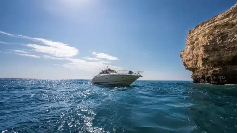 YOLO One luxury yacht cruising near large rocky cliffs in Marina de Vilamoura on a clear, sunny day, perfect for seafaring adventures.