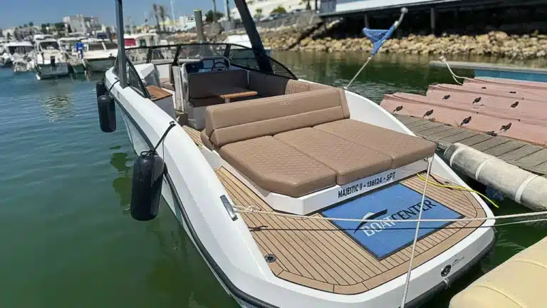 A modern bowrider boat with brown upholstery docked at a marina on a clear day with calm water and other boats in the background.