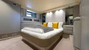 Luxurious bedroom interior on the yacht Katerina XL in Cascais Marina, featuring modern design with white and gray bedding accented by yellow pillows.