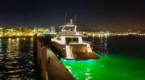 The yacht Katerina XL illuminated at night in Cascais Marina, surrounded by city lights and a Ferris wheel in the distance.