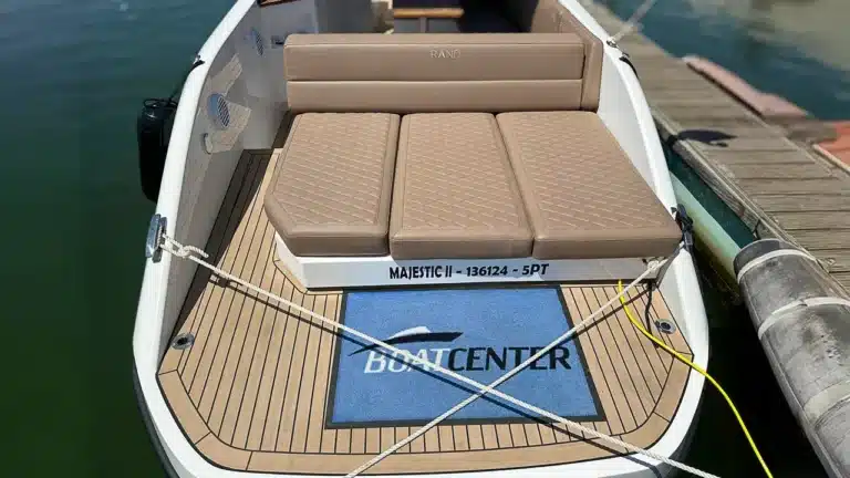 Rear view of a RAND yacht docked, featuring aft seating with brown cushions, teak-style deck flooring, and mooring ropes in a serene marina.