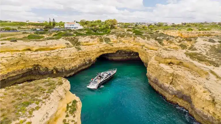 Baco IV yacht inside a coastal sea cave in Marina de Vilamoura with turquoise waters illuminated by skylight, surrounded by rocky cliffs.