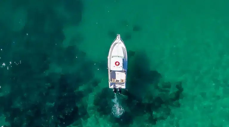 Aerial view of the Fishing Katerina, a white boat with a red circle symbol, on vibrant turquoise-to-emerald waters at Cascais Marina.