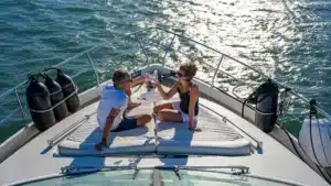 Two people on KEV yacht in Marina de Vilamoura toasting with wine glasses, enjoying a sunny day with scuba diving tanks in view.