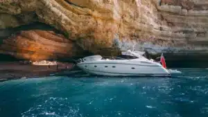 The YOLO One yacht near the shore inside a cave at Marina de Vilamoura with a sandy beach and turquoise water.